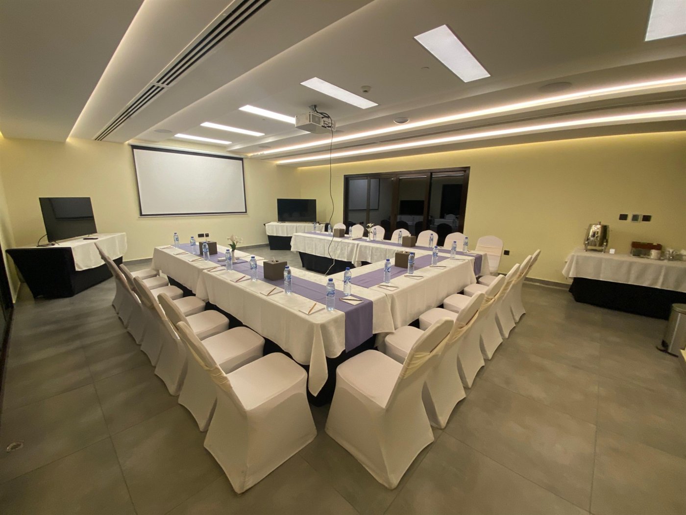 Indoor event hall with covered chairs, projector screen and TVs at Gul Café, Dubai Investment Park